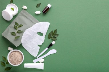 Kumaş kozmetik maske, kozmetik kil maske spatula ve fırça, tüp içinde nemlendirici krem, kavanoz. Yüz bakımı için güzellik spa tedavileri, yeşil arka planda kozmetoloji kopyalama alanı.