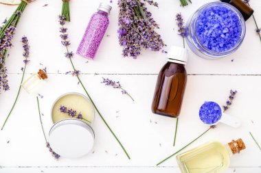 Lavanta eczanesi banyo ürünleri ve lavanta çiçekleri. Sabun, deniz tuzu, vücut yağı, masaj yağı, sıvı. Düz beyaz ahşap zemin. Cilt spa güzellik kozmetik.
