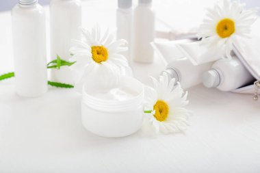 Nemlendirici cilt kremi için taklit beyaz plastik kavanoz, beyaz arka planda losyon. Beyaz kavanozda papatya çiçekli nemlendirici cilt kremi. Tüpler ve şişelerde beyaz cilt bakım ürünleri..