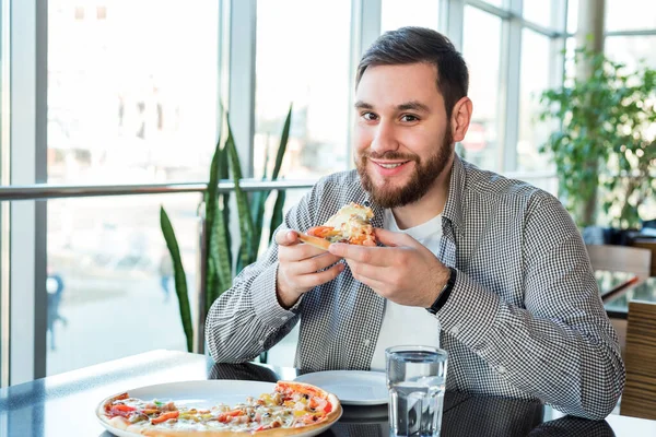 Happy smiling caucasian man eating Italian pizza in pizzeria keeps social distance. Delicious pizza in cafe