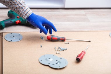 Erkek eli eldivenli, usta masa mobilyalarını tornavida aletleriyle topluyor, evde enstrüman kullanıyor. Tornavida kullanarak mobilya montajı. Taşınma, ev dekorasyonu, mobilya tamiri ve yenileme