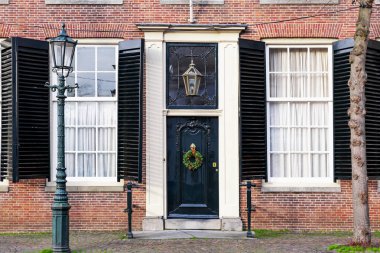 Sokak lambası ve Noel çelengi olan bir Noel verandası. Antika kapılı, antika pencereli ön kapılı ev cephesi. Şenlikli Noel dekoru olan siyah, eski bir kapı. Avrupa tarzı tuğla ev.