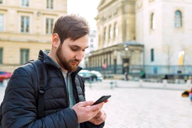 Akıllı telefondan bakan çekici, zeki genç bir adam. Avrupa 'da sokakta cep telefonu kullanan bir adam. Paris manzarası.