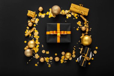 Altın kurdeleli siyah kağıda sarılı yeni yıl hediyesi kutusu. Noel şenlikli altın dekoru, karanlık arka planda toplara konfeti hediye etmek. Yeni yıl davetiyeniz kutlu olsun. Düz yatıyordu