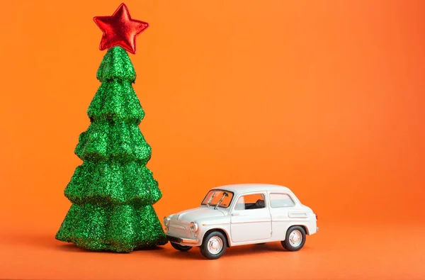 Arbre de Noël du Nouvel An avec étoile rouge sur le dessus près de jouet de voiture blanc. Arbre de Noël miniature créative et voiture sur fond de couleur orange.. Concept de livraison cadeau — Photo