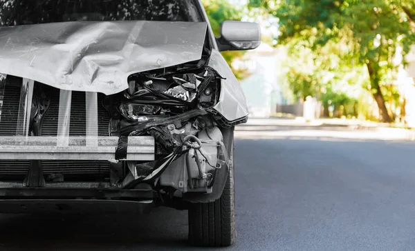 Destroyed car in car crash traffic accident on city road. Smashed broken auto headlight, dented hood without bumper in gray car accident with copy space. Auto life and health insurance. — Stock Photo, Image