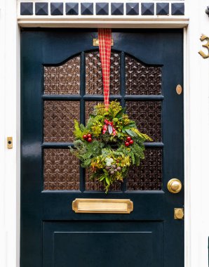 Kapının önünde Noel çelengi var. Veranda ön kapısı Noel şenlikli çelenk dekoruyla süslenmiş. Noel dış görünüşü