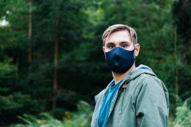 Siyah koruyucu maskeli adam dışarıda. Sadece orman manzarasında tıbbi maskeli adam portresi. Koronavirüse karşı koruma, salgın covid 19 hava kirliliği.