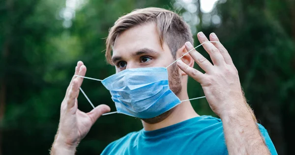 Man porträtt bär blå medicinsk mask i ansiktet. Vit man med kirurgisk engångs medicinsk mask mot coronavirus, epidemisk covid 19, smog luftföroreningar i parken ensam utanför. Lång web banner — Stockfoto