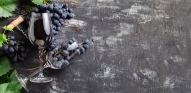 Kırmızı şarap ve üzümlü şarap bardakları. Koyu kırsal beton arka planda yaprakları ve sarmaşık mantarları olan üzüm demetleri. Düz şarap kompozisyonu siyah taş masa üzerinde yatıyordu. Kopyalama alanı olan uzun web pankartı.