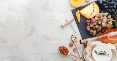 Gül şarabı, peynir, fındık, pembe ve siyah üzüm, tatlım. Camembert peyniri, şarap barı atıştırmalıkları. Açık gri kırsal beton arka planda şarap kompozisyonu. Kopyalama alanı olan uzun web pankartı.