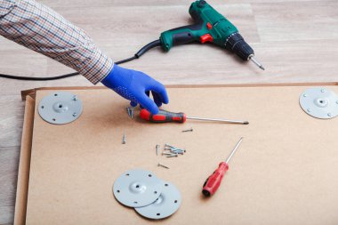 Erkek eli eldivenli, usta masa mobilyalarını tornavida aletleriyle topluyor, evde matkap aleti kullanıyor. Tornavida kullanarak mobilya montajı. Taşınma, ev tamiri, mobilya tamiri.