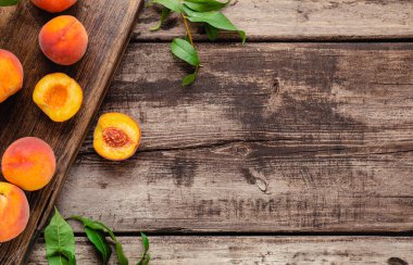 Tahtada yaprakları olan şeftalili şeftali. Olgun sulu şeftalilerle bezenmiş düz bir kompozisyon. Yiyecek ya da meyve suyu için şeftali hasadı. Fotokopi alanı olan taze organik meyveler.