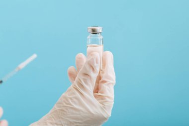 Cam şişe ve şırıngada Covid 19 aşı, doktor elinde ilaç sıvısı. Aşı aşıları mavi arka planda tedavi olarak kullanılıyor. Covid 19 Sağlık Hizmetleri Tıbbi Bağışıklık Konsepti.