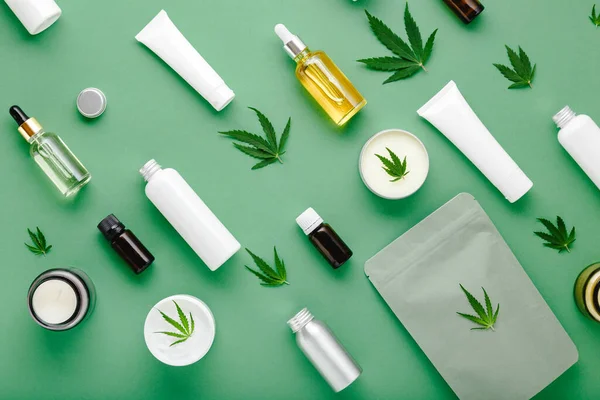 Cam damlası şişesinde kenevir yağı serumu, kenevir yaprağı, nemlendirici krem, serum, losyon, gerekli yağ. Cilt kozmetik ürünü olan kenevir yaprağı yeşil arkaplanda düz bir desen oluşturdu