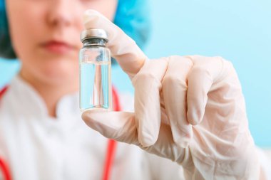 Cam şişe içinde Covid 19 aşı, doktor elinde ilaç sıvısı stetoskopla eldiven. Aşı enjeksiyonları mavi arka planda tedavi ediliyor. Covid 19 bağışıklık kavramı