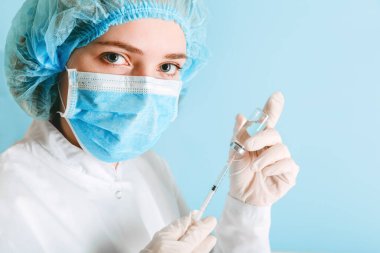 Hemşire şırıngaya iğne yapmak için kovid 19 aşı koyuyor. Coronavirus aşısı. Doktor kadın tıbbi koruyucu maske ve eldiven takarak mavi arka planda fotokopi alanı ile kapak aşısı yapıyor.
