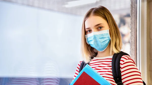 Estudante em máscara médica protetora. Retrato de estudante loira perto da janela da universidade durante o bloqueio vívido do coronavírus. Banner web longa com espaço de cópia — Fotografia de Stock