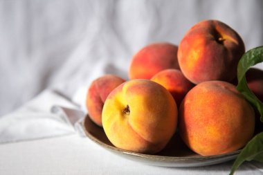 Yapraklı şeftaliler... Masada yeşil renkli, beyaz masa örtülü bir hayat. Olgun sulu şeftaliler. Hâlâ hayat. Yemek için şeftali hasadı. Taze organik meyve.