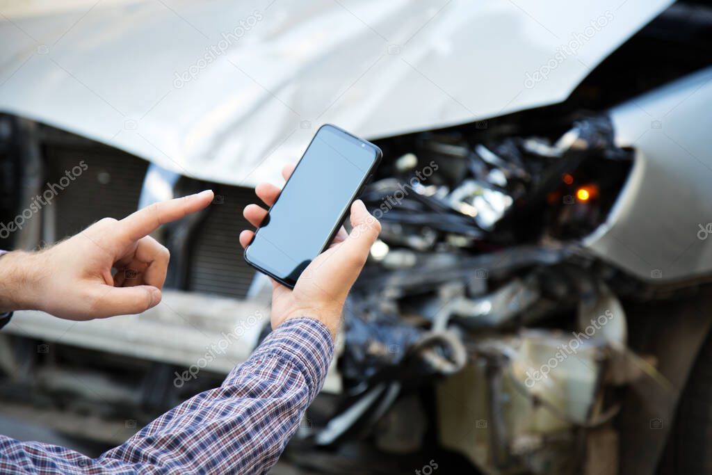 Man holds mockup mobile phone screen in hands after car accident. Calling insurance service in web app to place of car accident. Smartphone in front of wrecked car