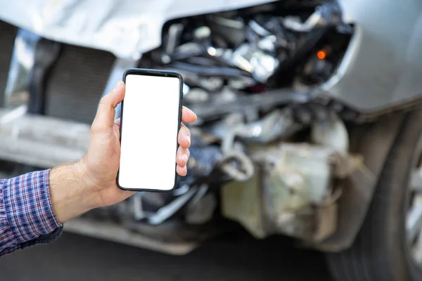 White mockup screen mobile phone in male hands after car accident. Mock up for Insurance service, driving school, tow truck call or web app above car accident. Smartphone in front of wrecked car