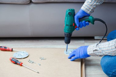 Elektrikli matkap evde tamircinin elinde çalışıyor. Erkek eller eldiven giyip mobilyaları monte etmek ve tamir etmek için elektrikli matkap kullanıyor. Ev yapımı. Boşluğu kopyala