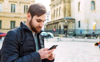 Akıllı telefondan bakan çekici, zeki genç bir adam. Avrupa 'da sokakta cep telefonu kullanan bir adam..