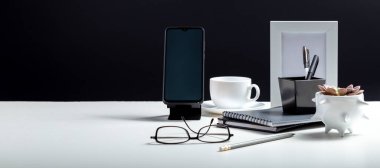 İçişleri Bakanlığı çalışma alanı. Akıllı telefon şablonu boş olan bir masaüstü, not defterleri ofis kalemleri, kahve fabrikası tedarikçileri. Siyah arka planda beyaz çalışma masası. Kopyalama alanı olan uzun web pankartı.