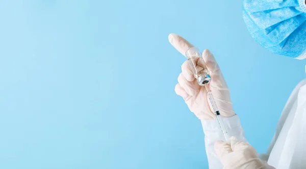 Médico haciendo la vacunación con máscara protectora y guantes. Covid 19 Vacuna en frasco de vial de vidrio y jeringa, medicamento líquido en la mano del médico para inyección. Banner web largo con espacio de copia en azul. — Foto de Stock