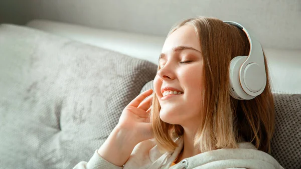 Happy young woman sitting on sofa in headphones. Woman or teen girl resting, bliss enjoy listening to music on couch in living room. portrait of woman resting with closed eyes. Long web banner.