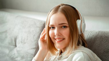 Kanepede oturan, kulaklıklı mutlu genç bir kadın. Kadın ya da genç kız dinleniyor, mutluluk oturma odasının iç tarafındaki kanepede müzik dinlemekten zevk alıyor. Dinlenen kadın portresi. Uzun web pankartı.