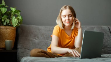 Düşünceli beyaz kadın evden bilgisayarla uzaktan kumandayla çalışıyor. Oturma odasında internetten ders çalışan genç kız öğrencinin portresi. Dizüstü bilgisayarla uzaktan eğitim. Uzun web pankartı.