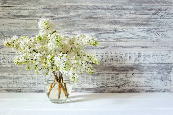 White lilac bouquet in glass vase on wooden table. Spring branches of blooming lilac festive bouquet of flowers with copy space