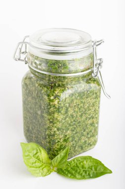 Cam kavanozdaki pesto sosu beyaz arka planda taze fesleğen yapraklarıyla izole edilmiş. Geleneksel ev yapımı İtalyan sosu ve fesleğen.