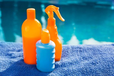 Kozmetik güneş kremi ürünleri, farklı turuncu güneş koruyucu vücut kremlerini mavi havuza ve yüzme havuzuna koyun. Cilt bakımı ve koruma konsepti. Altın ten rengi. Tasarım için boşluk, kopyalama alanı