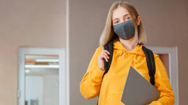 Sırt çantalı maskeli kız öğrenci. Koruyucu tıp maskeli genç bayan öğrenci. Coronavirus covid lockdow sırasında üniversitenin içindeki sarışın kız öğrenci portresi. Uzun web pankartı
