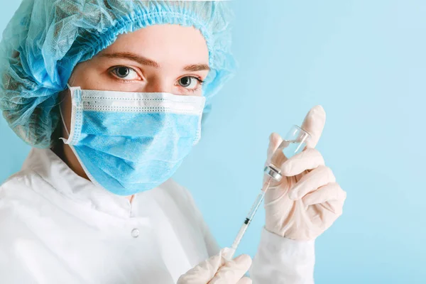 Portrait of doctor or nurse during coronavirus vaccination. Woman puts covid 19 vaccine into injection syringe . Doctor in medical protective mask and gloves on color blue background with copy space