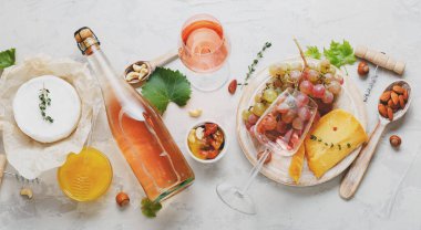 Güvertede servis edilen lezzetli şarap aperatifleri. Pembe şarap, gül, peynir, peynir, fındık, bal, üzüm, şarap. Açık gri beton zemin üzerinde düz uzun web afişi serili