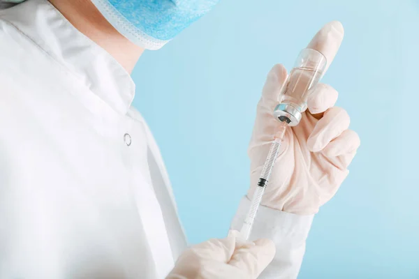 Nurse in white uniform medical protective mask gloves make Covid vaccination on color blue background. Doctor puts covid 19 vaccine into syringe to make injection. Coronavirus vaccination