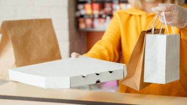 Paket pizza, paket pizza kahve, yemek teslimatı. Eldivenli kadın paket servis siparişleriyle çalışıyor. Garson yemek hazırlarken şehir merkezi 19, koronavirüs kapanıyor. Uzun web pankartı..