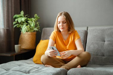 Ev içi akıllı telefon kullanarak internet 'te sörf yapan ciddi sakin bir kadın. Genç sarışın hippi kız kanepede mesajlaşarak sohbet ediyor. Genç kadın çevrimiçi iletişim için mobil uygulama kullanıyor