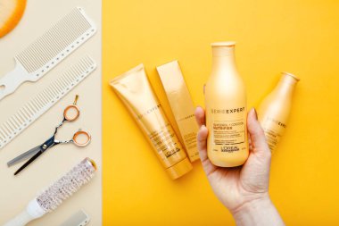 L 'oreal Profesnel Paris Serie Expert loreal besleyici saç ürünleri makas tarakları ve kuaför aletleri. Renkli arka planda el şampuanı. Altın kozmetik şişeleri.