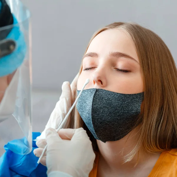 Coronavirüs kovid 19 hastalarının teşhisi. Koruyucu tıbbi maskeli doktor nazofaringeal kültürü kadınlara test ediyor. Hemşire pamuklu çubukla tükürük testi yaptırdı.