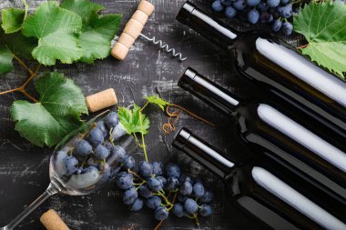 Kırmızı şarap şişeleri üzümler, üzüm yaprakları ve sarmaşık mantarları koyu kırsal beton arka planda şarap bardakları. Siyah taş tebeşir masasında şarap kompozisyonu. Üst görünüm