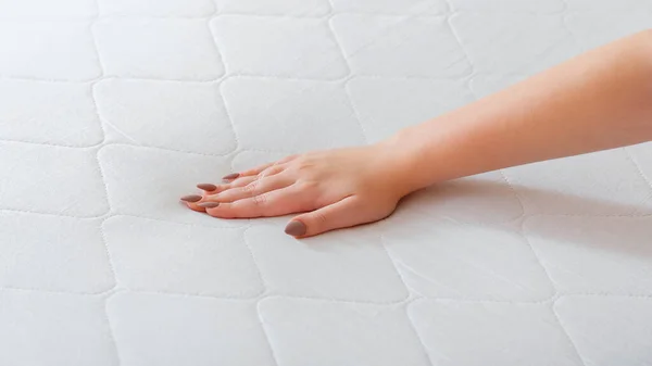 Yeni yatak seçen bir kadın. Yumuşaklığı kontrol etmek için kadın eli baskı yapıyor. Mağazada uyumak için rahat bir yatak seç. Beyaz şiltenin kalite kontrol sertliği. Uzun web pankartı.