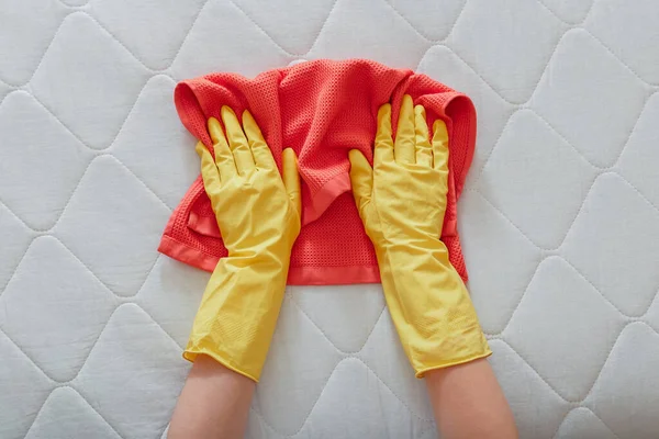 Employee cleans surface of mattress on bed with rag. Cleaning disinfection surfaces. Cleaning company person Hands in rubber gloves do Mattress chemical cleaning