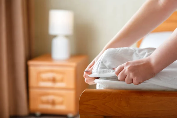 Woman puts on new mattress pad on mattress corner. Bed linen at home or hotel. Sheet is worn on soft clean white mattress. Protection from dirt and washed linens mattress pad in bedroom interior