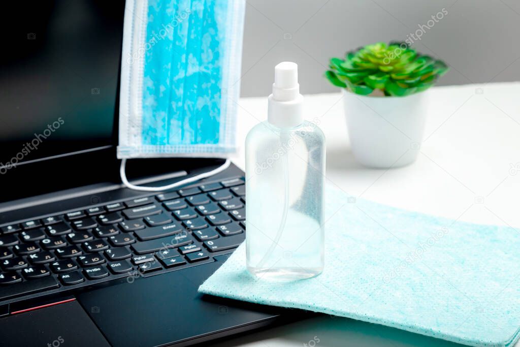 Disinfectant spray laptop medical protective mask on work space as New Normal covid 19 coronavirus hygiene. Alcohol sanitizer on napkin laptop keyboard. Cleaning surfaces pc keyboard work space table.
