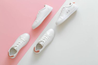 Pembe arka planda beyaz erkek ve kadın spor ayakkabıları. Kopya alanı olan beyaz deri ayakkabılar. İki şık spor ayakkabı rahat spor giyim hippi kadın ayakkabısı.