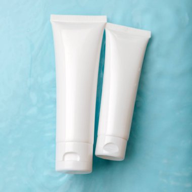 Su yüzeyindeki cilt kozmetik paketlerini taklit et. Doğal nemlendirici su kozmetik güzellik ürünü. Mavi arka planda beyaz kozmetik ürünler ve damlalar. kare.